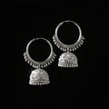 Silver hoop earrings with dangling parts on a black stand, branded 'Saheli'.