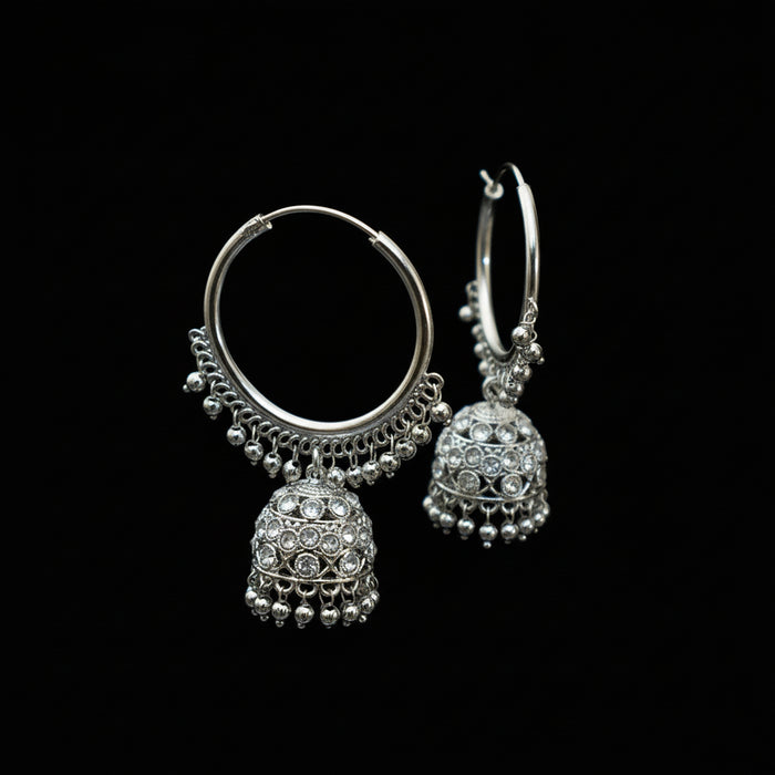 Silver hoop earrings with jhumka designs on a black stand against a dark background
