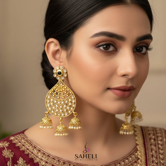 Gold earrings with intricate designs on a dark background, featuring the brand 'Saheli'.