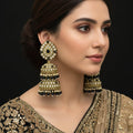 Gold and black earrings on a stand with 'Saheli' branding.