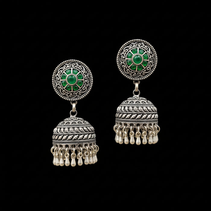 Ornate silver earrings with green stones on a gray stand, branded 'Saheli'.