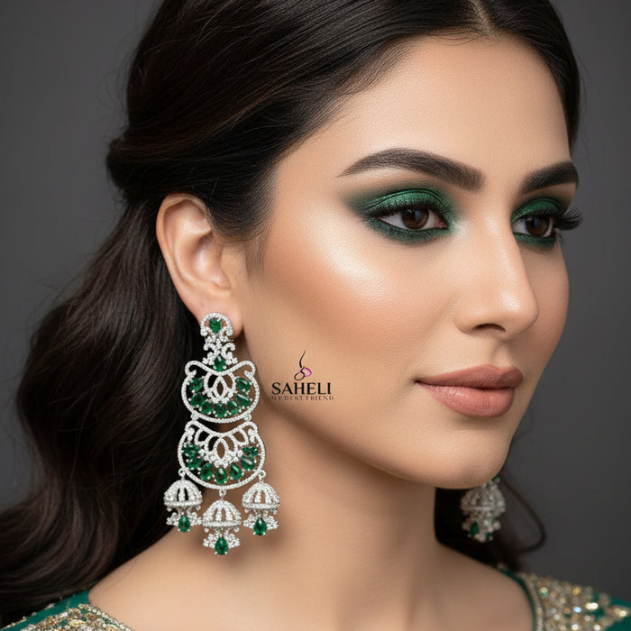 Pair of silver earrings with green gemstones on a gray background, branded 'Saheli'.