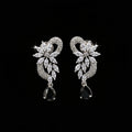 A pair of silver-tone drop earrings with clear marquise and round stones forming a floral heart design, each ending in a black teardrop stone, displayed on a black stand against a gray background. The brand logo 'SAHELI MY BEST FRIEND' is visible in the top left corner.