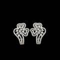 A pair of silver-toned statement earrings with intricate pavé detailing, displayed on a black stand against a dark gray background with the brand logo 'SAHeli' at the top.
