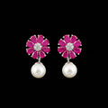 A pair of flower-shaped drop earrings with bright pink gemstone petals, silver-toned metal settings with clear stones in the center, and hanging white pearl drops, displayed on a black stand against a gray background. The brand name 'SAHELI MY BEST FRIEND' is visible at the top.