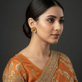 Gold earrings with red gemstones on a dark background, branded 'Saheili'.