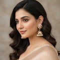 Gold and pearl earrings on a gray stand with 'SAHELI' branding.