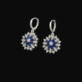 Pair of silver earrings with blue and white stones on a gray background, branded 'Saheli'.