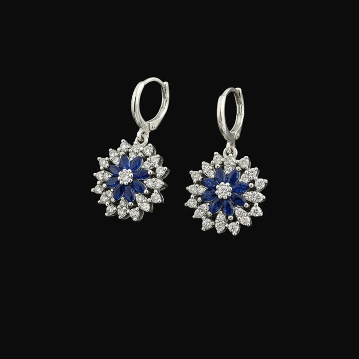 Pair of silver earrings with blue and white stones on a gray background, branded 'Saheli'.