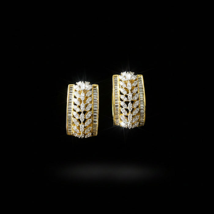 A pair of gold hoop earrings adorned with pavé-set clear stones and channel-set side stones, displayed on a dark reflective surface with the brand logo 'SAHELI MY BEST FRIEND' above them.