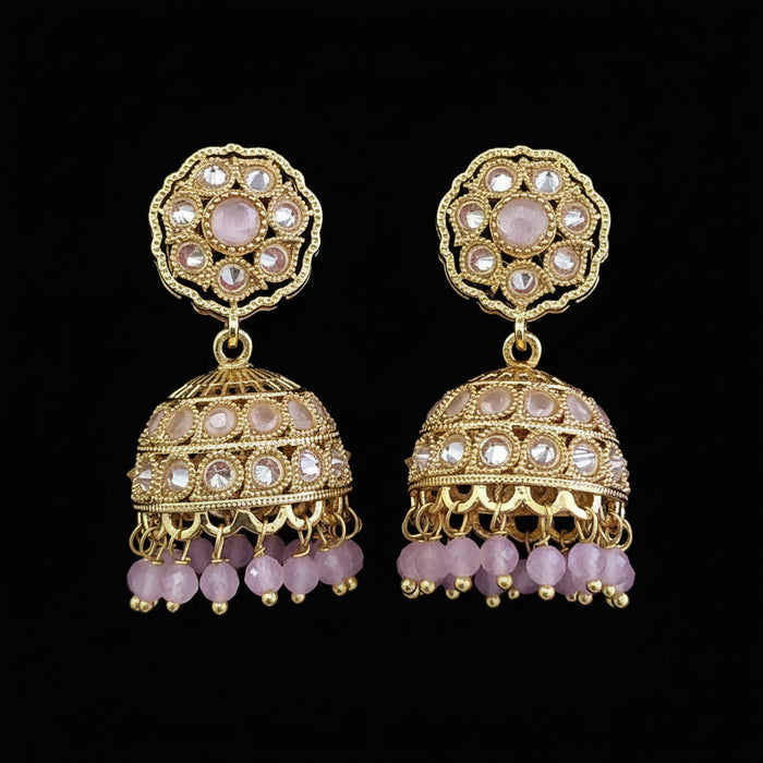 A pair of ornate gold-toned jhumka earrings embellished with clear stones and pink beads, displayed on a solid dark pink background.
