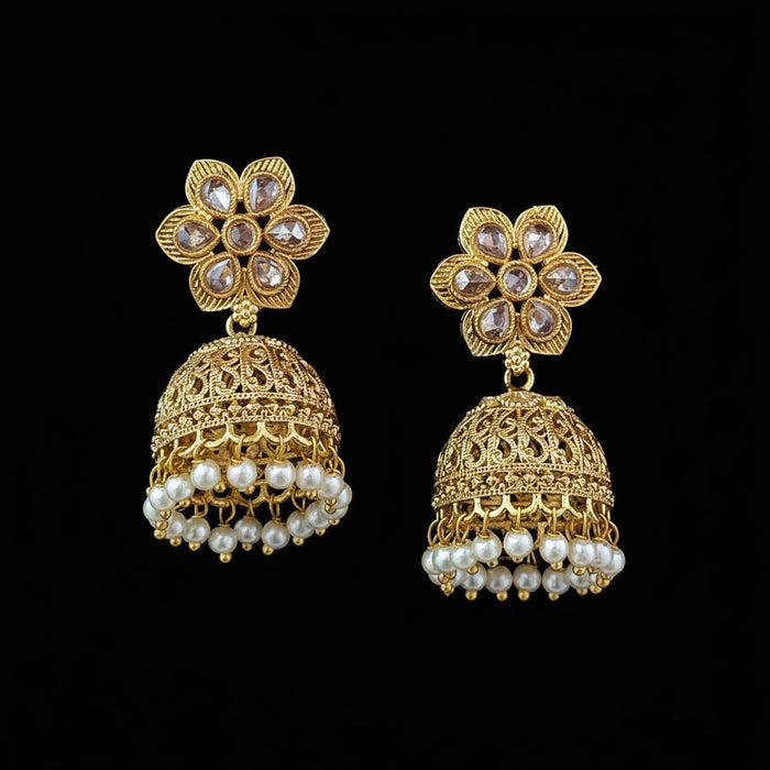 A pair of gold-plated Indian jhumka earrings with floral stud tops, clear rhinestones, and dangling pearl bead fringes, displayed on a solid dark purple background.