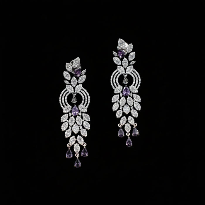 A pair of ornate silver-toned dangle earrings embellished with clear pavé stones and accented with purple amethyst teardrop and round stones, displayed on a dark gray background.