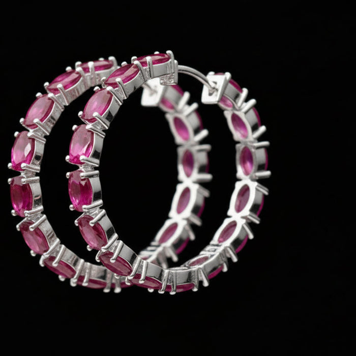 Gold hoop earrings with pink gemstones on a black background