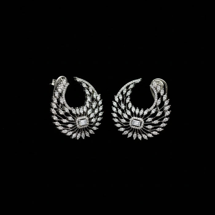 A pair of silver-toned crescent-shaped earrings adorned with numerous clear stones, featuring a central square-cut stone, displayed on a dark gray background.