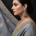 Pair of ornate earrings with blue stones and pearl-like elements on a dark background