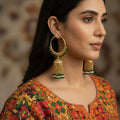 Gold hoop earrings with green beads on a black background, branded 'Saheli'.
