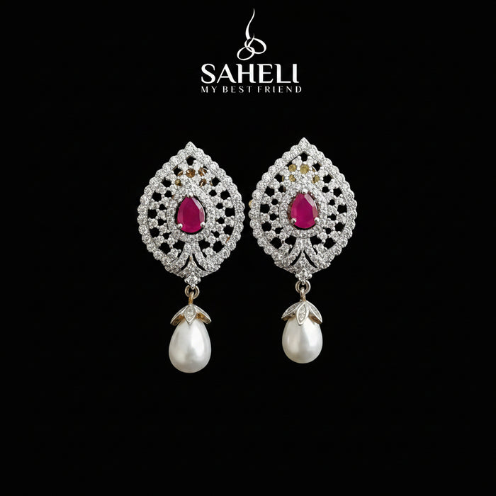 A pair of ornate silver-toned drop earrings with bright pink teardrop-shaped center stones and dangling white pearl drops, displayed on a black stand against a gray background. The brand name 'SAHELI MY BEST FRIEND' is visible at the top.