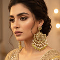 Pair of gold and pearl earrings with green stones on a dark background