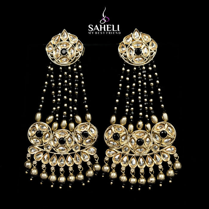 Ornate gold earrings with black stones on a black background, featuring the brand 'Saheli'.