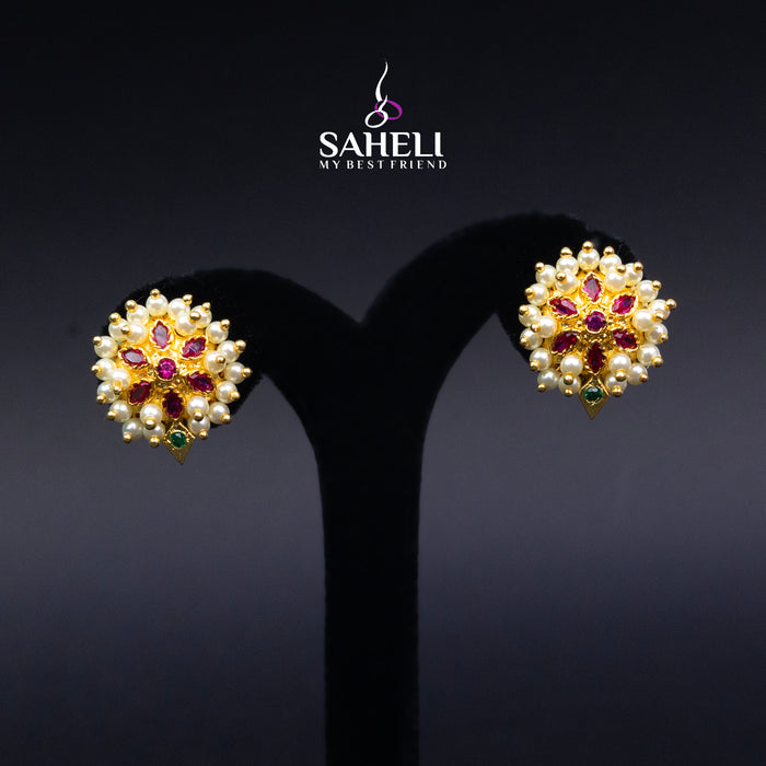Gold earrings with gemstones on a black stand, branded 'Saheli'.