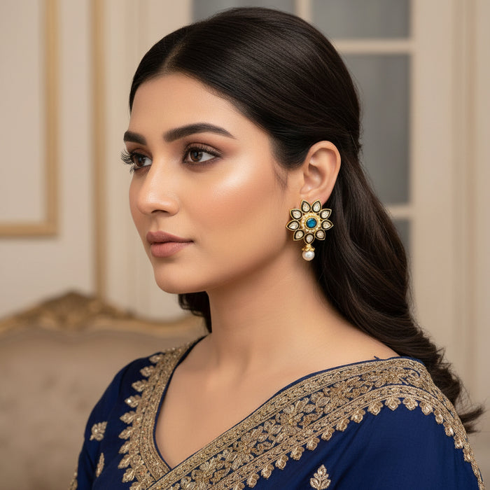 Decorative earrings with gold, blue, and pearl details on a dark background, featuring the brand 'Saheli'.