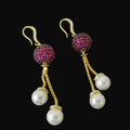 Pair of earrings with pink gemstones and pearl drops on a dark background, branded 'Saheli'.