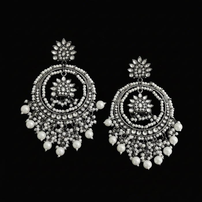 A pair of ornate silver-toned dangle earrings with intricate circular beadwork, floral motifs, and dangling pearl-like beads, displayed on a dark reflective surface.