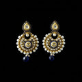 A pair of ornate Indian jhumka earrings with gold-plated metalwork, white pearl beads, blue enamel details, and dark blue teardrop dangling charms, displayed on a dark gray reflective surface with the 'SAHELI MY BEST FRIEND' logo at the top.
