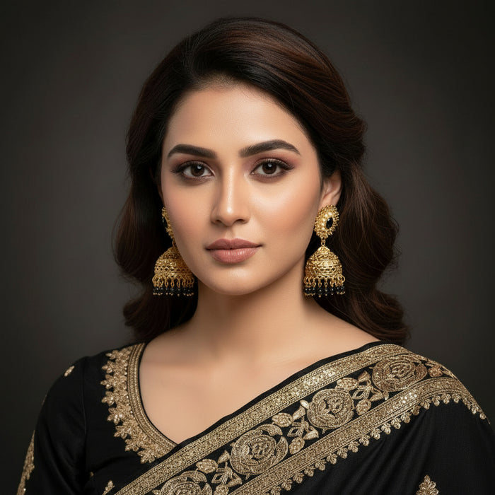 Woman wearing a pink saree with gold embroidery and jhumka earrings against a dark background