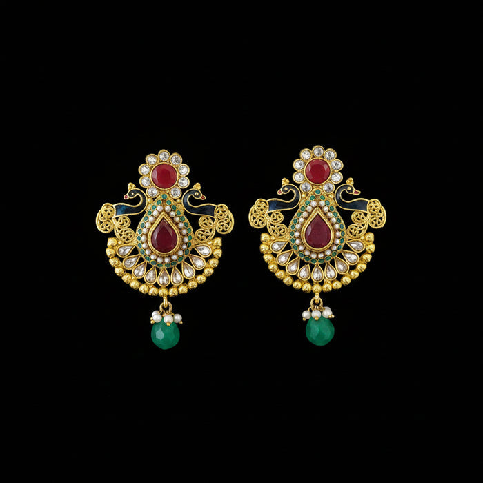 A pair of traditional Indian gold-plated earrings with red stones, green bead drops, and white stone accents, displayed on a dark gray reflective surface with the brand name 'SAHELI MY BEST FRIEND' printed above.