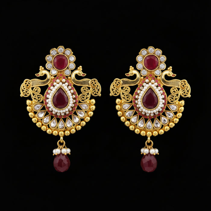 A pair of traditional Indian gold-plated earrings with red stones, white faux pearls, and black enamel details, displayed on a gray background with a 'SAHELL MY BEST FRIEND' watermark.