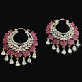 Pair of ornate earrings with red gemstones and gold accents on a dark background, branded 'Saheli'.