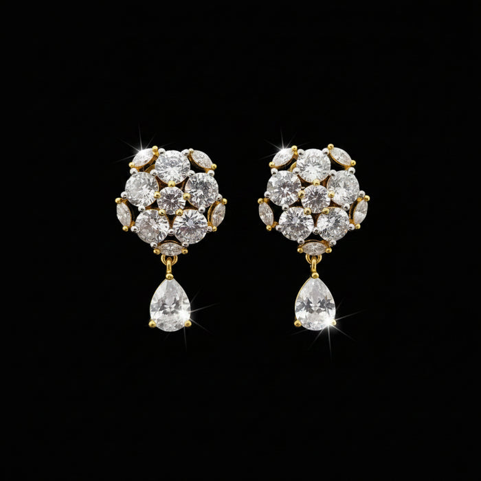 A pair of gold-toned statement earrings with clear gemstones, displayed on a black stand against a gray background with the brand name 'SAHELI MY BEST FRIEND' at the top.