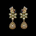 A pair of gold-plated Indian Kundan earrings with green enamel, white faux pearls, and clear crystals, displayed on a black Y-shaped stand against a gray background with the brand logo 'SAHeli My Best Friend' in the center.