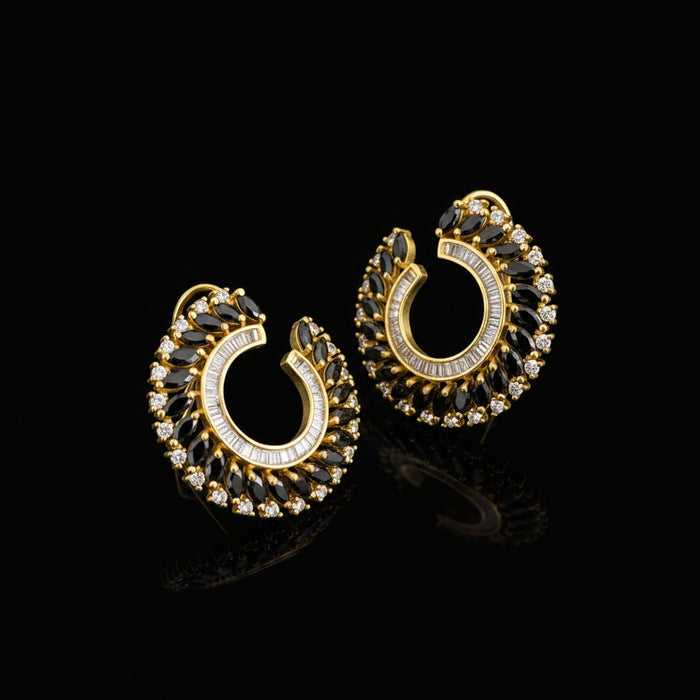 A pair of gold crescent-shaped hoop earrings adorned with clear crystals and dark marquise-cut stones, displayed on a dark reflective surface with the brand logo 'SAHELL MYBESTFRIEND' visible above.