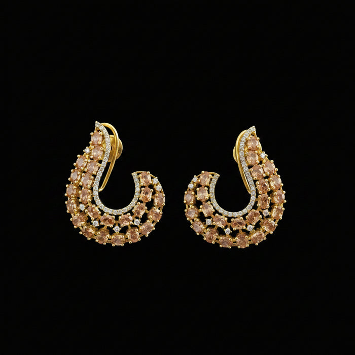 A pair of gold-toned crescent-shaped earrings embellished with small clear stones and accented with warm yellow stones, displayed on a dark reflective surface with the SAHELI MY BEST FRIEND logo above.