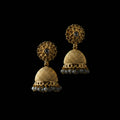 Gold jhumka earrings on a gray stand with a blurred background