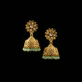 Gold floral earrings with green stones on a black stand against a dark background