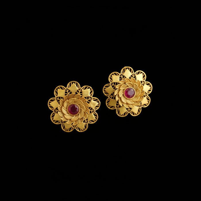 Pair of gold flower-shaped earrings with red centers on a dark background