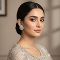 Pair of diamond earrings on a dark background with 'Saheli' branding.