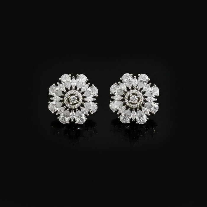 Pair of diamond earrings on a dark background with 'Saheli' branding.