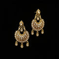 A pair of ornate gold-toned dangle earrings with clear stones, displayed on a gray stand against a gray background with the brand name SAHELI MY BEST FRIEND printed above.