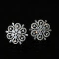 Pair of silver floral earrings on a black background with 'SAHELI' branding.