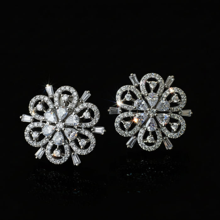 Pair of silver floral earrings on a black background with 'SAHELI' branding.