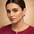Pair of ornate earrings with a pink gemstone on a gray background, branded 'SAHELL'.