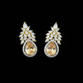 A pair of gold and silver stud earrings featuring pear-cut orange gemstones surrounded by clear crystals, displayed on a dark reflective surface with a Saheli logo in the top left corner.