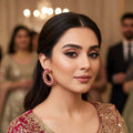 Ornate earrings with pink and gold details on a gray background, featuring the brand 'Saheli'.