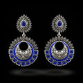 Ornate silver and blue earrings on a stand with 'SAHELI' branding.