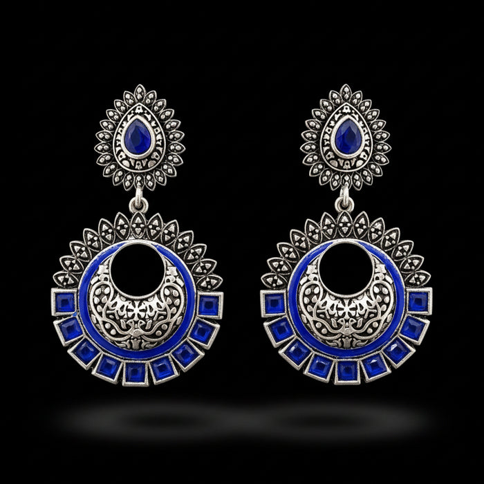 Ornate silver and blue earrings on a stand with 'SAHELI' branding.